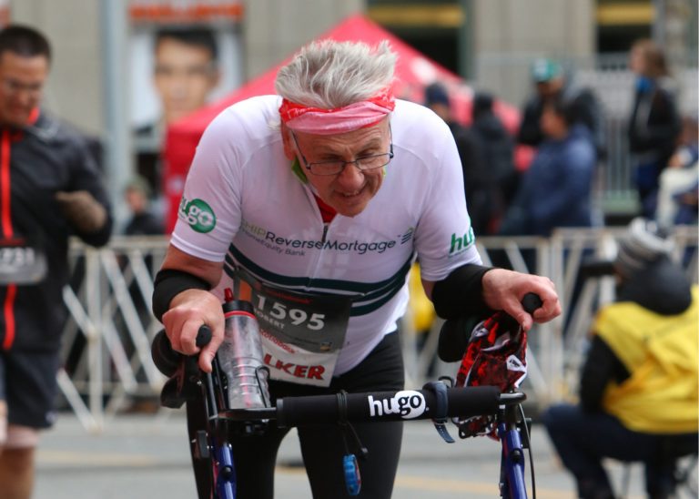 A photo of Robert Bob Hardy The Walker Runner, speed walking at the Toronto Marathon in October 2018 with his walker. Photo by Toronto Marathon, used on the website bobhardythewalkerrunner.com, designed and hosted by Evolvingmedia.com
